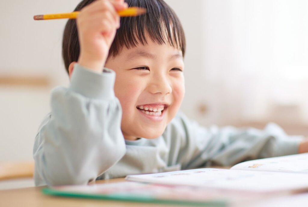 幼児の男の子が右手で鉛筆を持ち笑顔で机に座る画像
